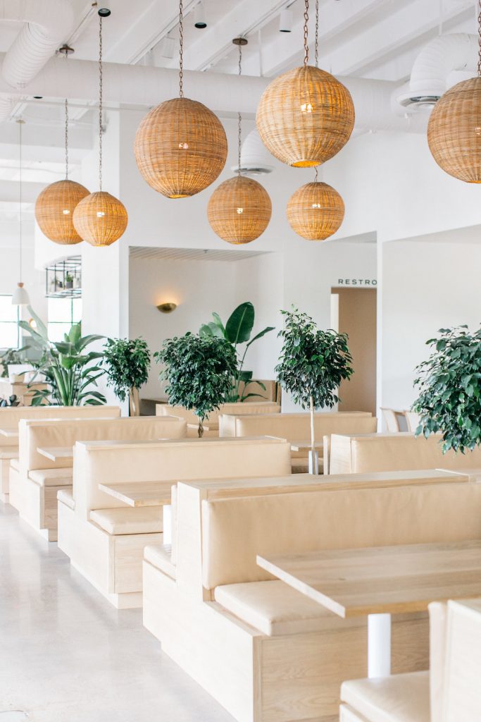 Light wood booths with green trees and natural woven lanterns at Hank's in Austin, Texas.