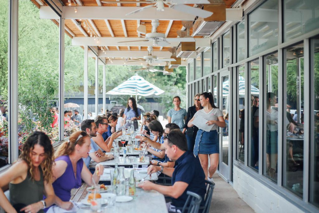 People eating at marble tables on busy patio at Launderette in Austin, Texas.