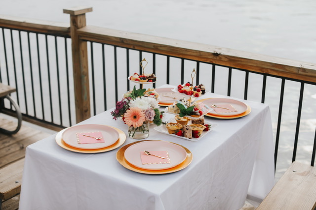 Picnic table with a white tablecloth, pastries, pink plates, and a bouquet of flowers next to the water at Mozart's Coffee Roasters in Austin, Texas.