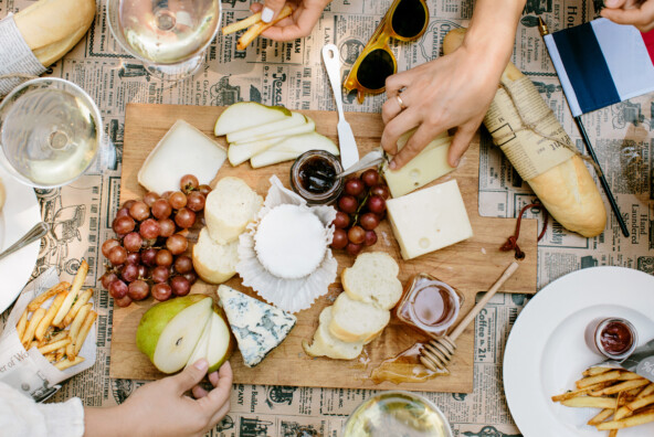 Cheeseboard with pear slices, grapes, honey, and different cheeses on newspaper-covered table.