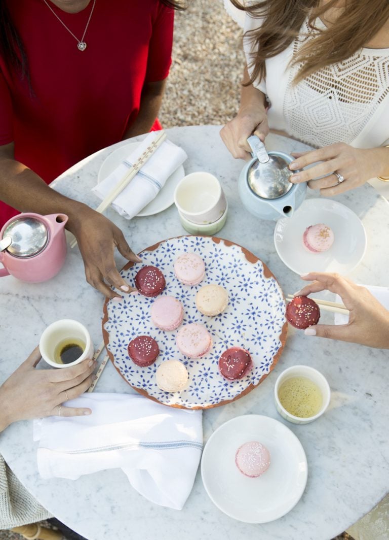 Mujeres comiendo macarrones y bebiendo té en una mesa de mármol.