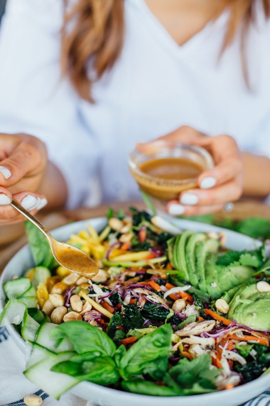 pouring dressing on thai chicken salad
