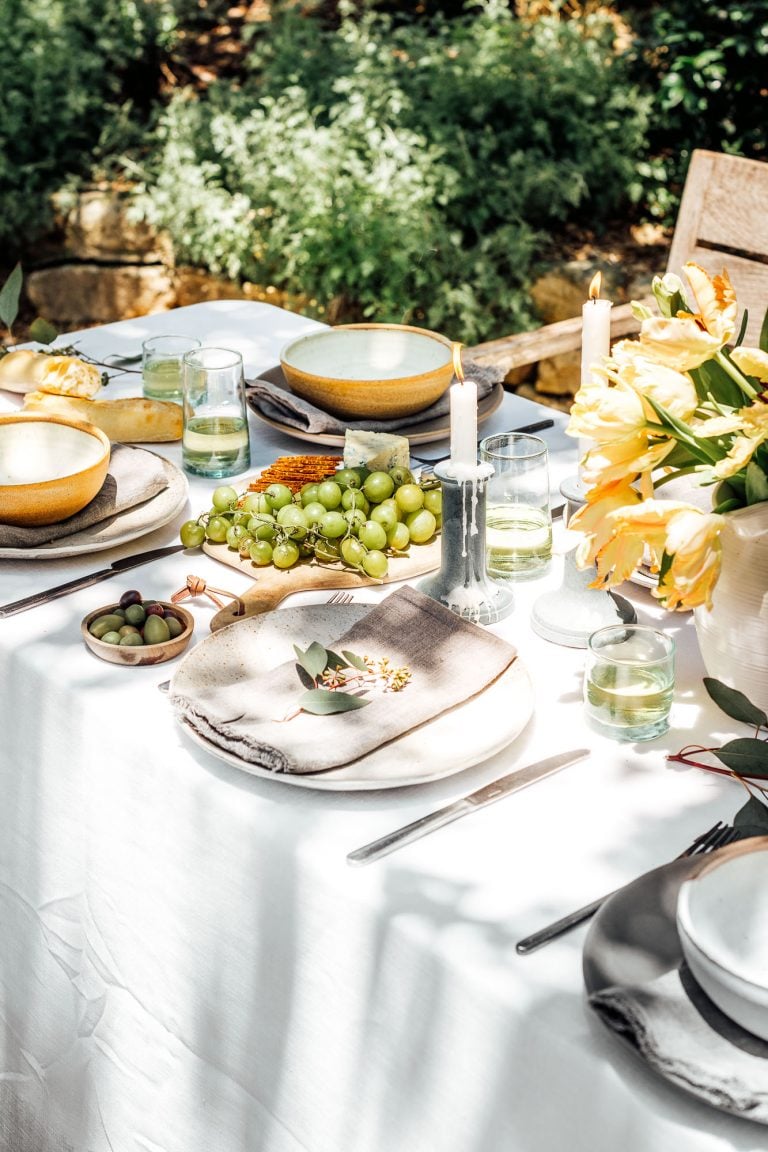 summer table setting ideas, Camille Styles summer dinner party table in backyard with trees, grapes and candlesticks, spring flowers