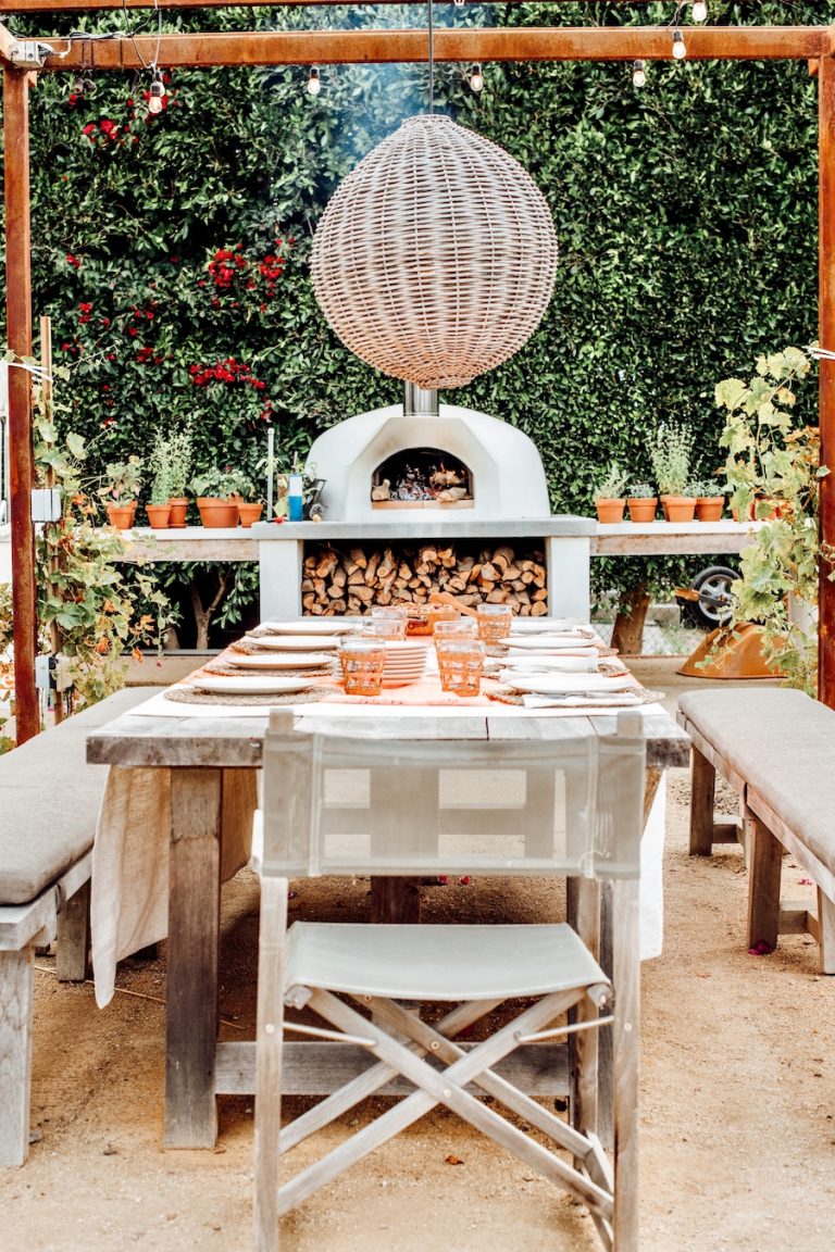 Covered outdoor dining table pergola with woven light fixture pendant, pizza oven, dinner party at malibu farm