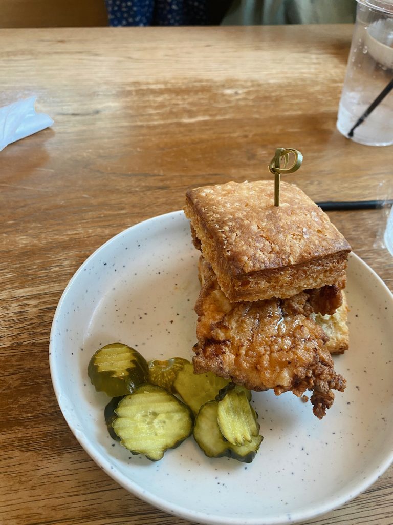 Fried chicken biscuit sandwich and pickle chips on speckled white plate at Better Half Coffee & Cocktails in Austin.
