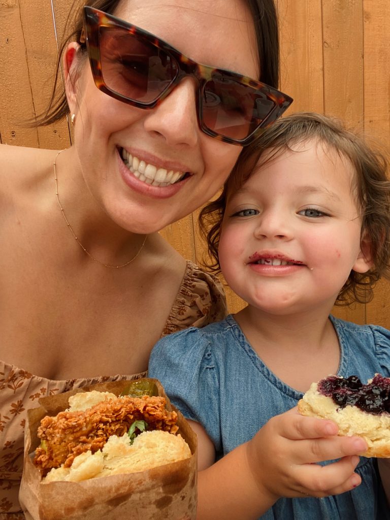Mother and young daughter smiling with fried chicken sandwich at Bird Bird Biscuit in Austin.