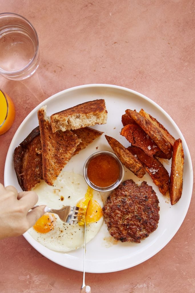 Breakfast at Paperboy in Austin. White plate with toast, sausage, eggs, potatoes, and ketchup.