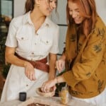 Two women smiling while topping dark chocolate bark — feel-good dessert making in progress