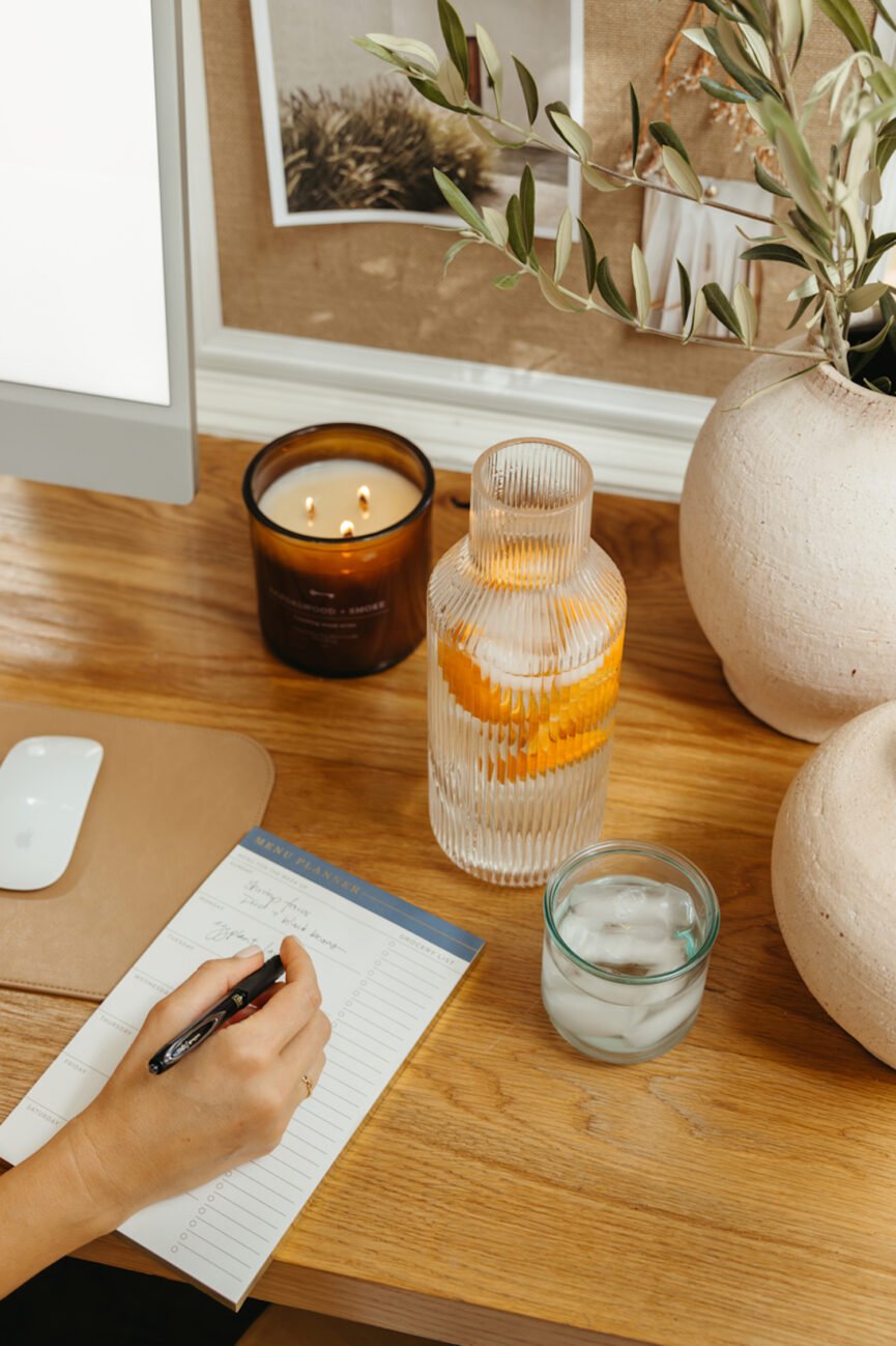 Woman writing plant-based meal prep on weekly menu planner.