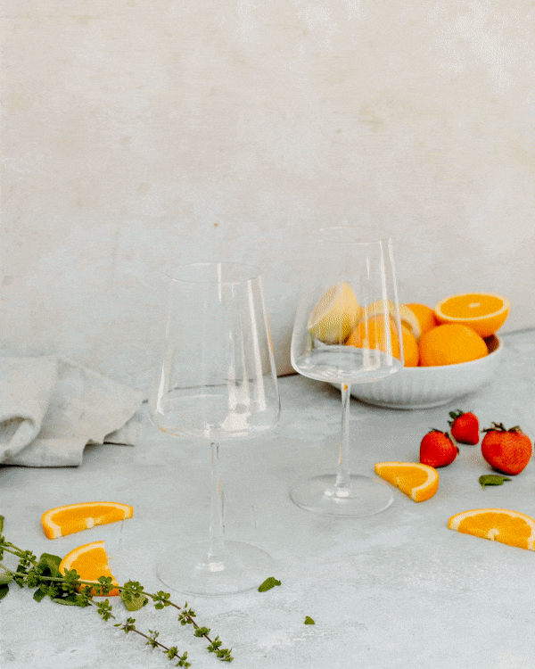Strawberry rosé was poured into two wine glasses alongside a bowl of oranges and strawberries.