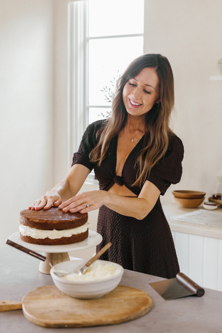 Camille Styles decorating carrot cake in bright kitchen.