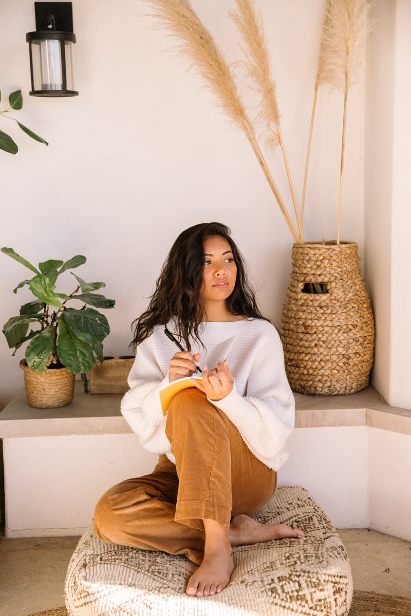 A woman journaling outside on a meditation pillow.