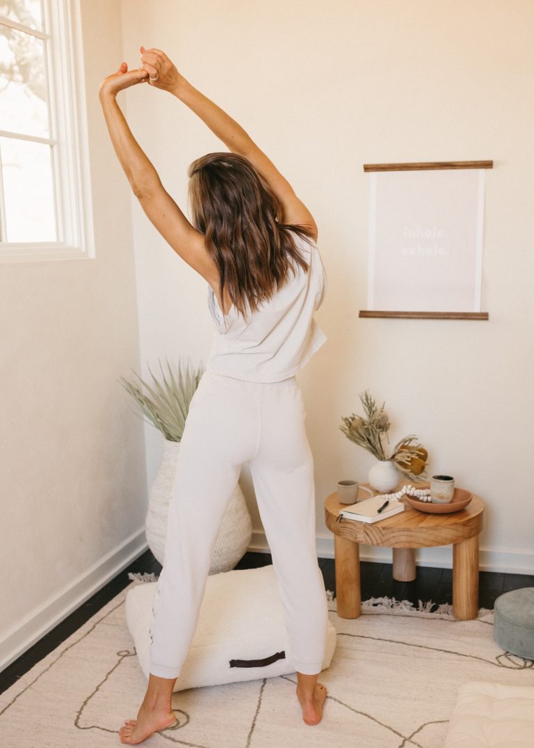 Woman stretching and raising arms above head in calming, meditative space_emotional exhaustion