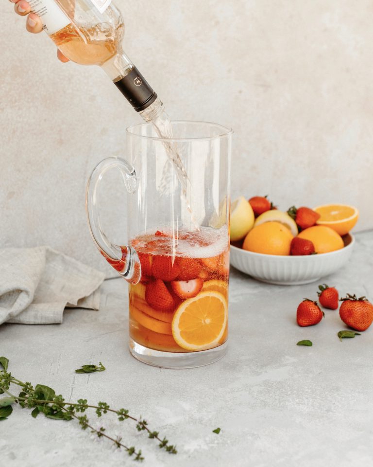 Vase of strawberry pink sangria recipe next to a bowl of strawberries and oranges 