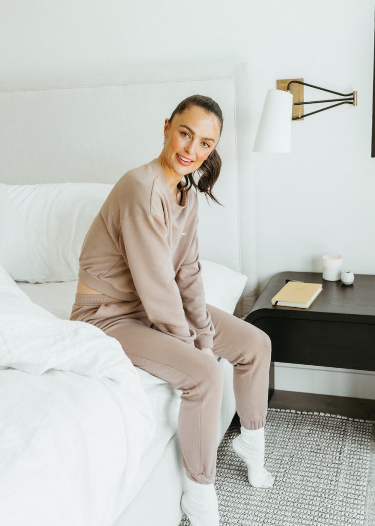 Megan Roup at home in her bedroom wearing a mauve-colored sweatsuit and white socks_best affordable luxury sheets