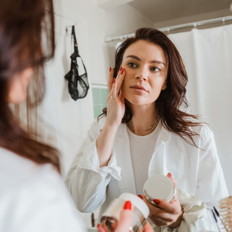 woman applying skincare at bathroom mirror