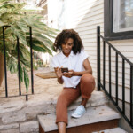Woman sitting on house stoop using phone outside_best period tracker apps