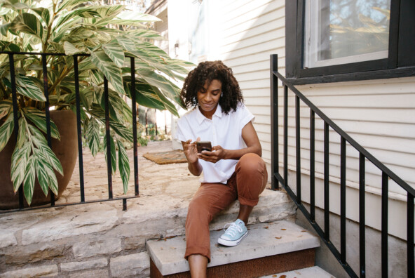 Woman sitting on house stoop using phone outside_best period tracker apps