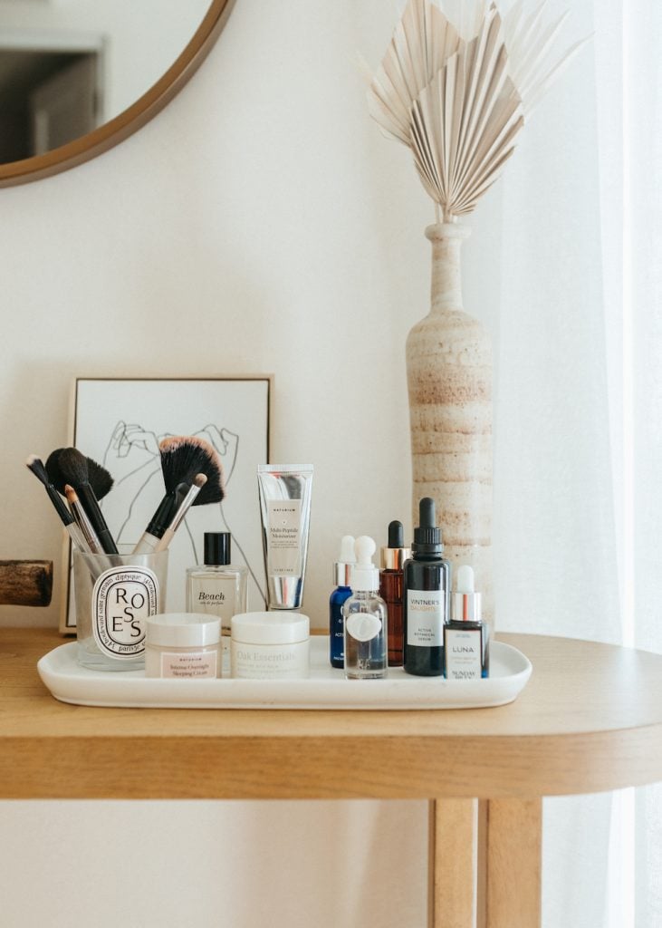 Beauty products on white tray sitting on light wood console table.