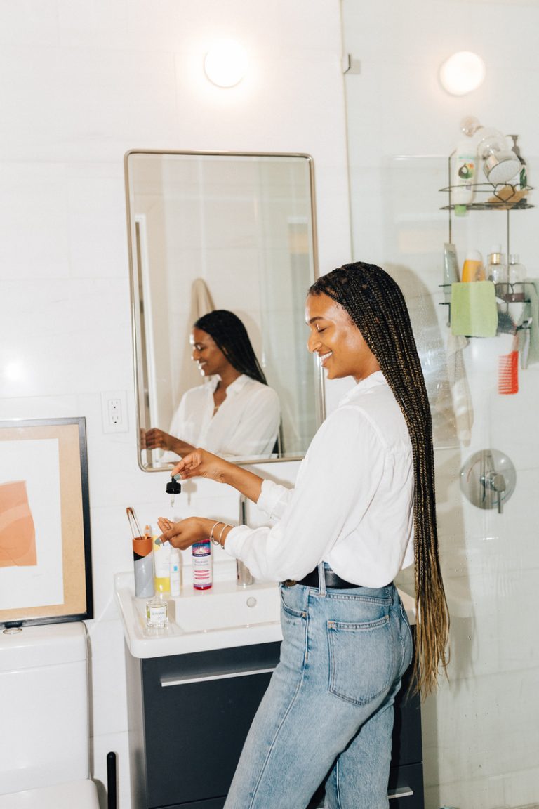 Woman applying skincare serum in bathroom mirror.