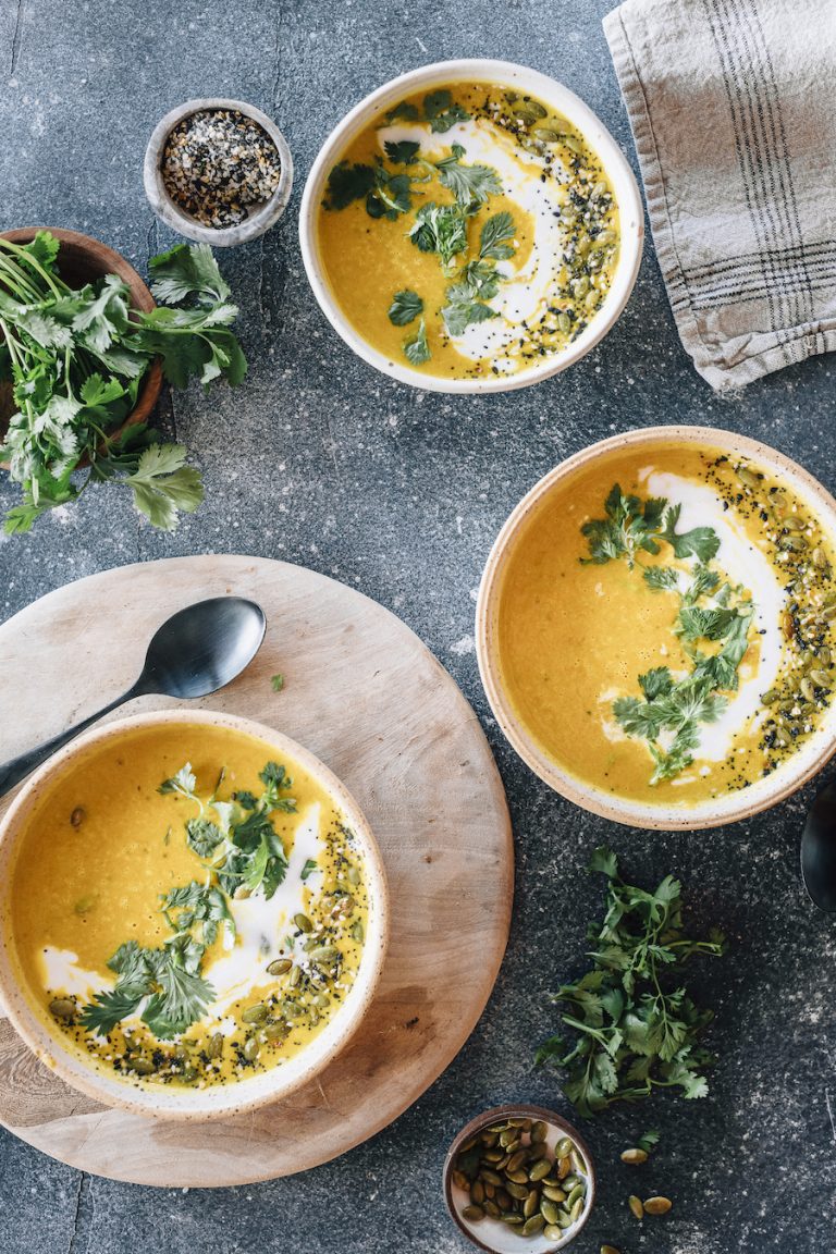 two bowls of butternut squash soup with coriander and seeds
