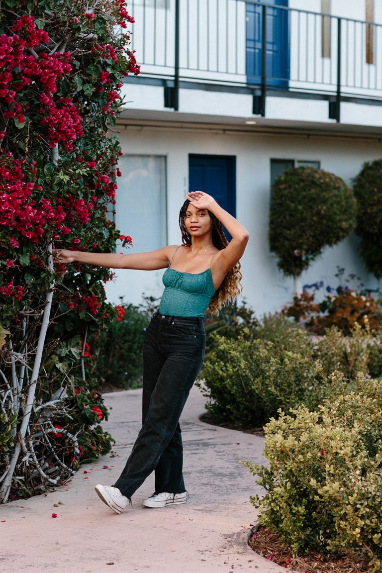 Black women wearing green tank top and black jeans posing outside.