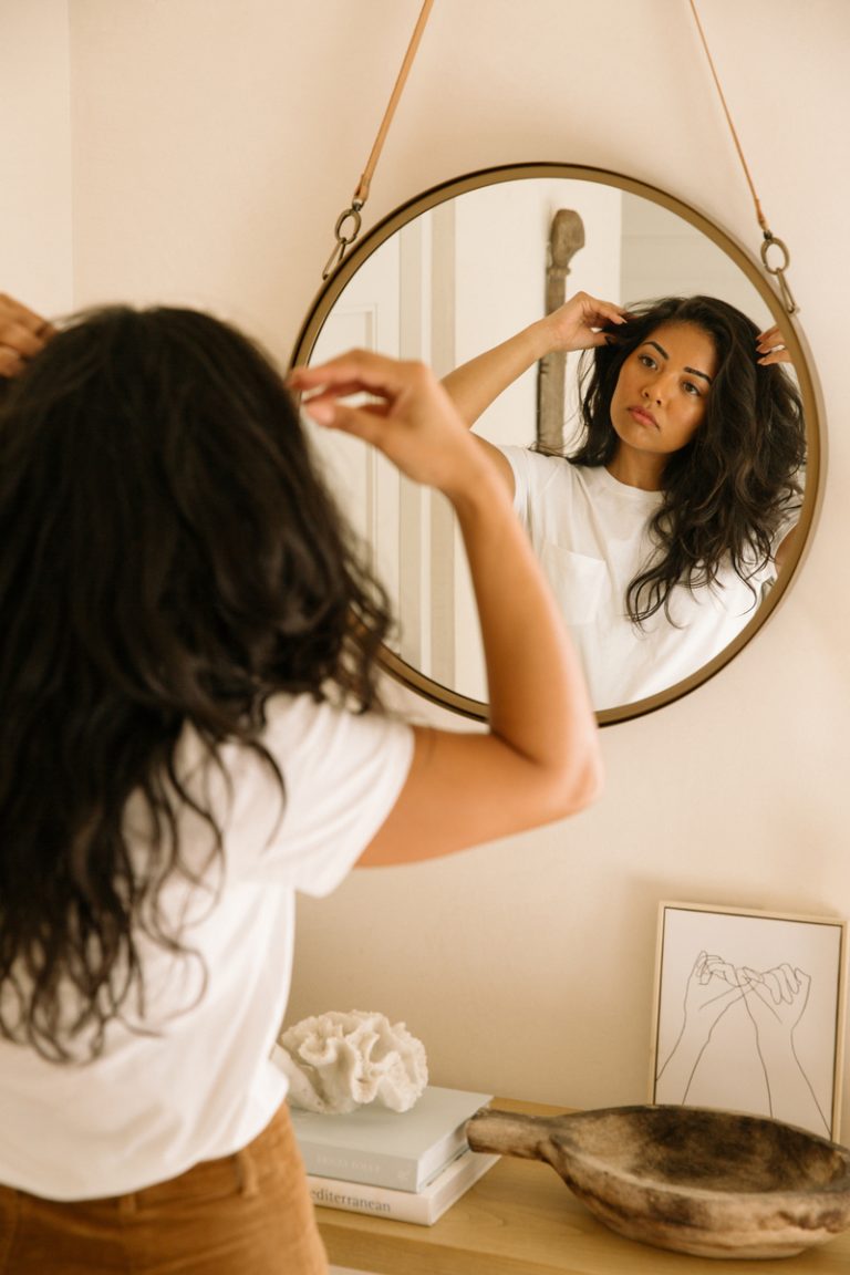 woman looking in mirror touching hair_perfectionism and anxiety