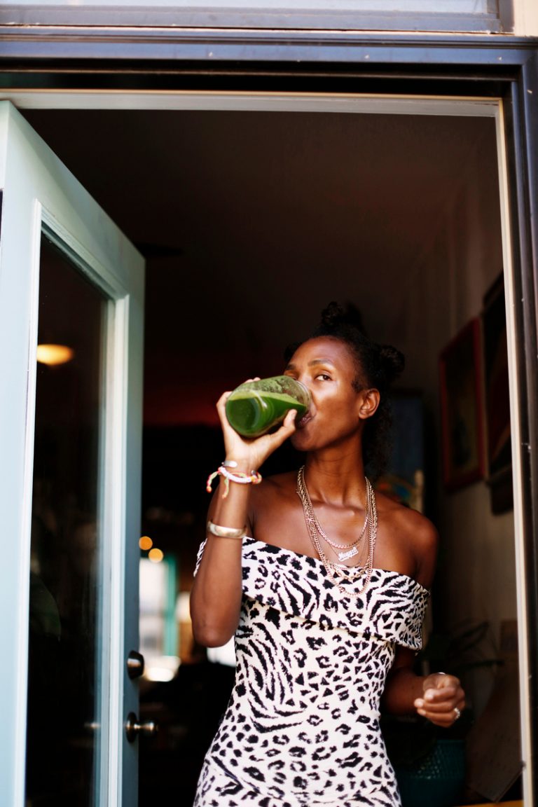 Black woman wearing zebra print off-the-shoulder dress drinking green juice.