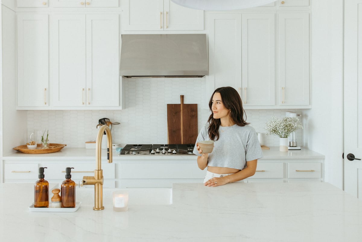 Woman drinking matcha at kitchen counter.