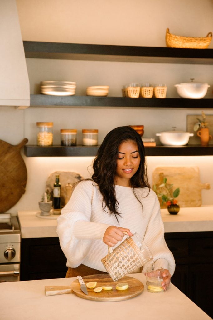 Woman pouring lemon water into cup in kitchen.