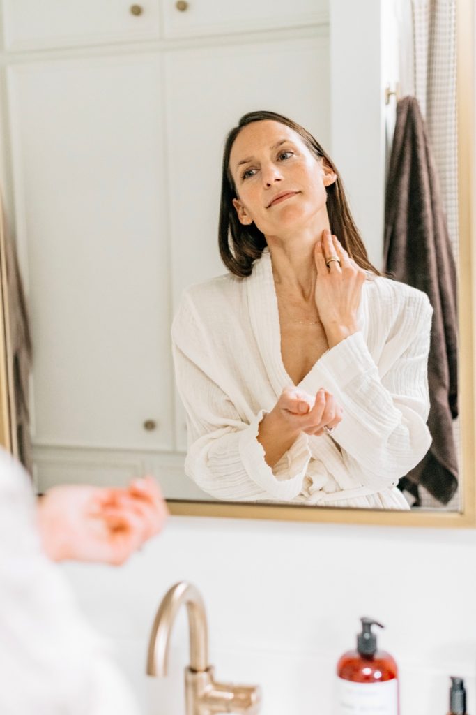 woman applying neck cream in mirror_best way to apply skincare