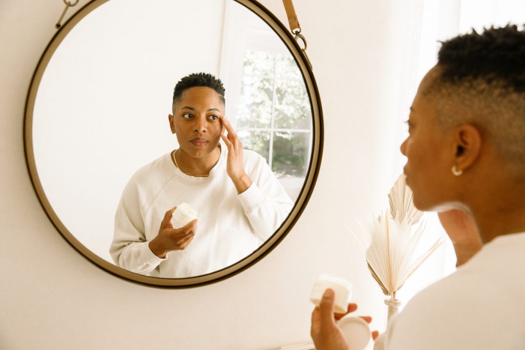 woman applying eye cream in mirror_best way to apply skincare