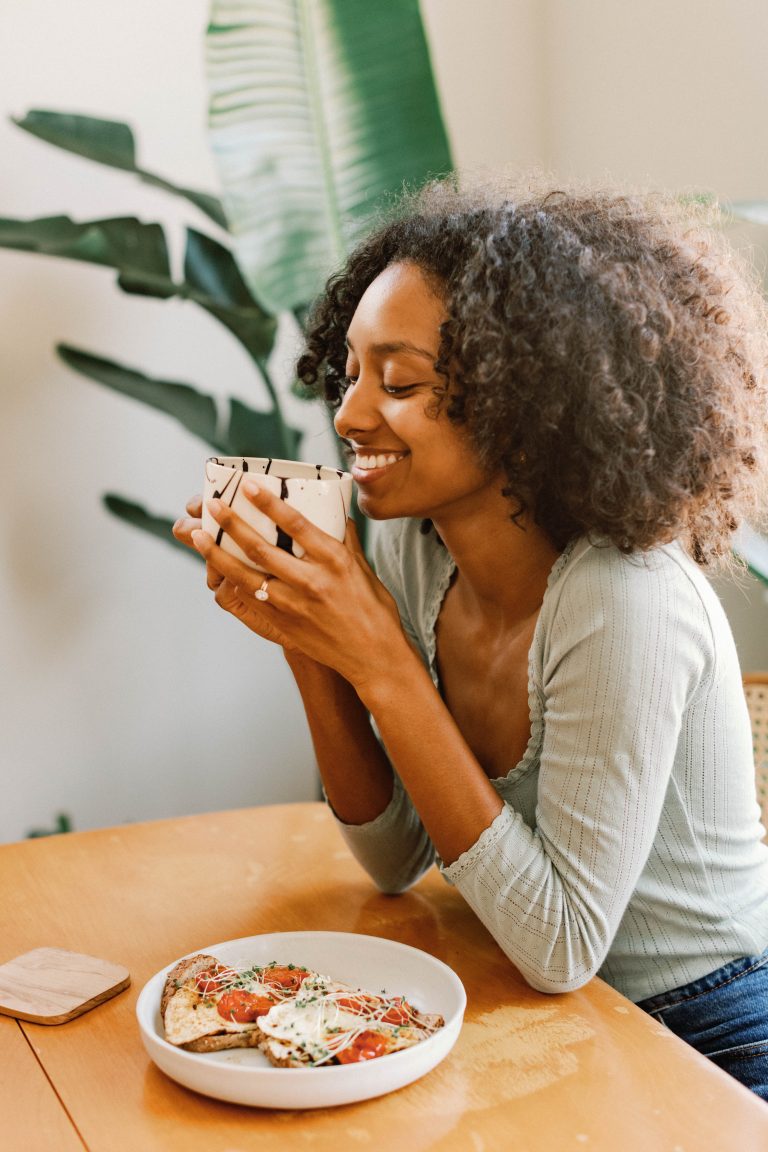 Woman drinking coffee and eating eggs and toast.