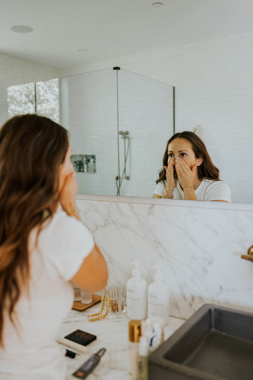 Woman using face oil in mirror.