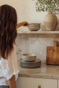 woman putting away ceramics on organized kitchen shelves