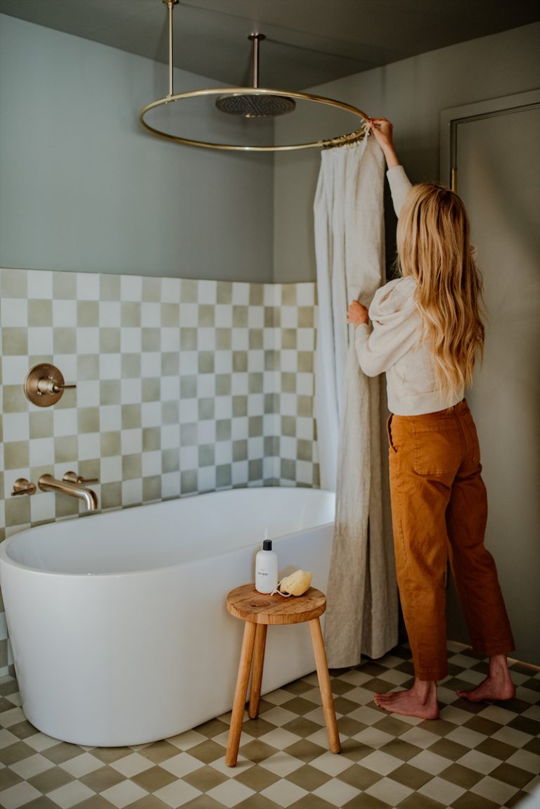 Woman stringing shower curtain in quirky, modern bathroom.