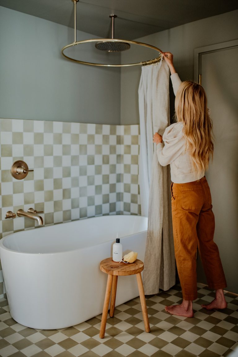 A woman pulling up a shower curtain in a quaint modern bathroom.