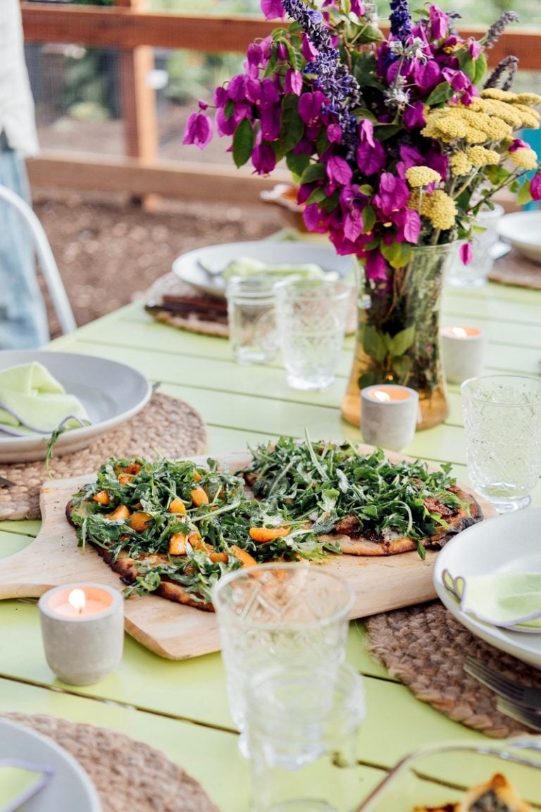 Pizza with arugula on a pizza crust on an outdoor table.