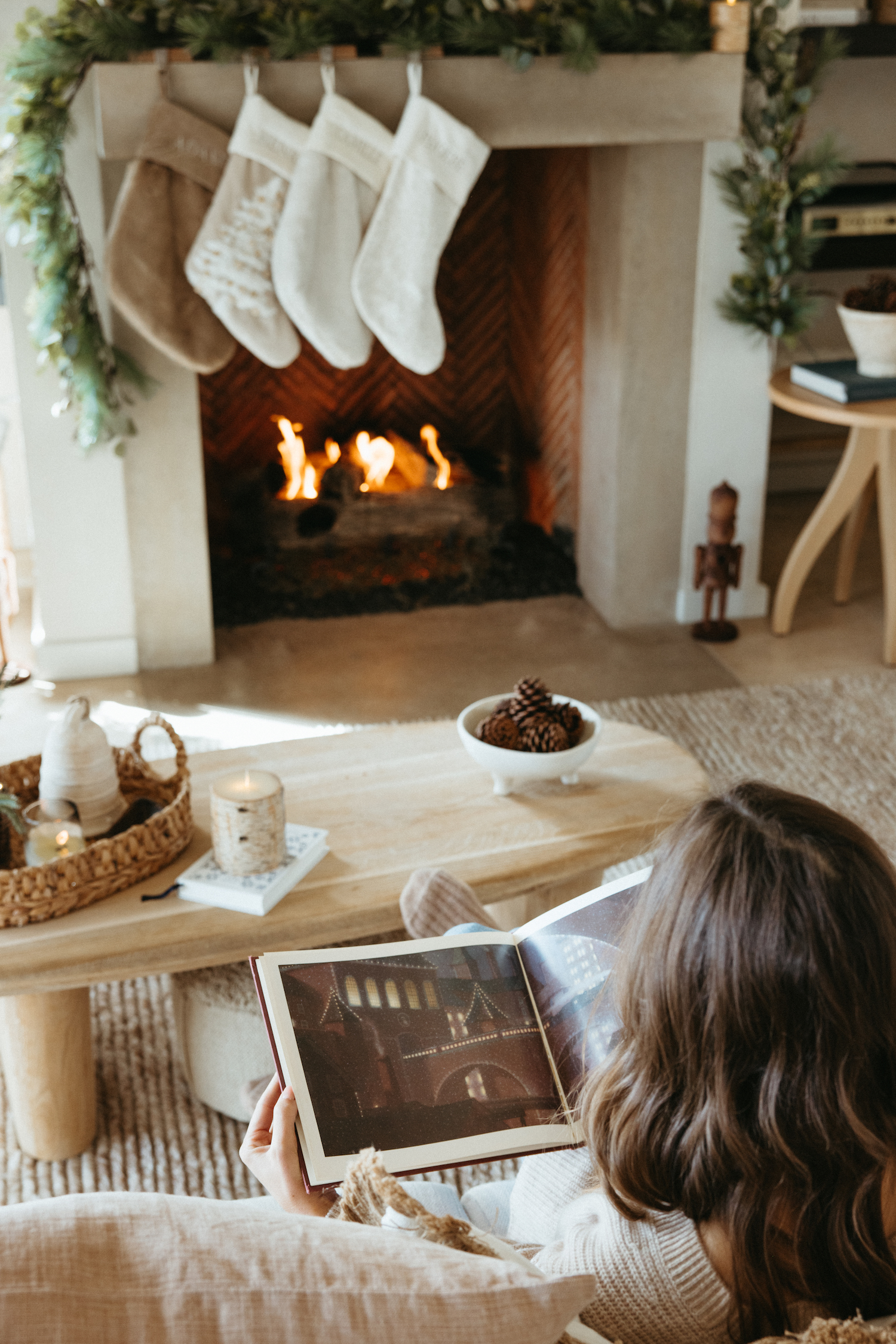 Woman reading book in front of fireplace.
