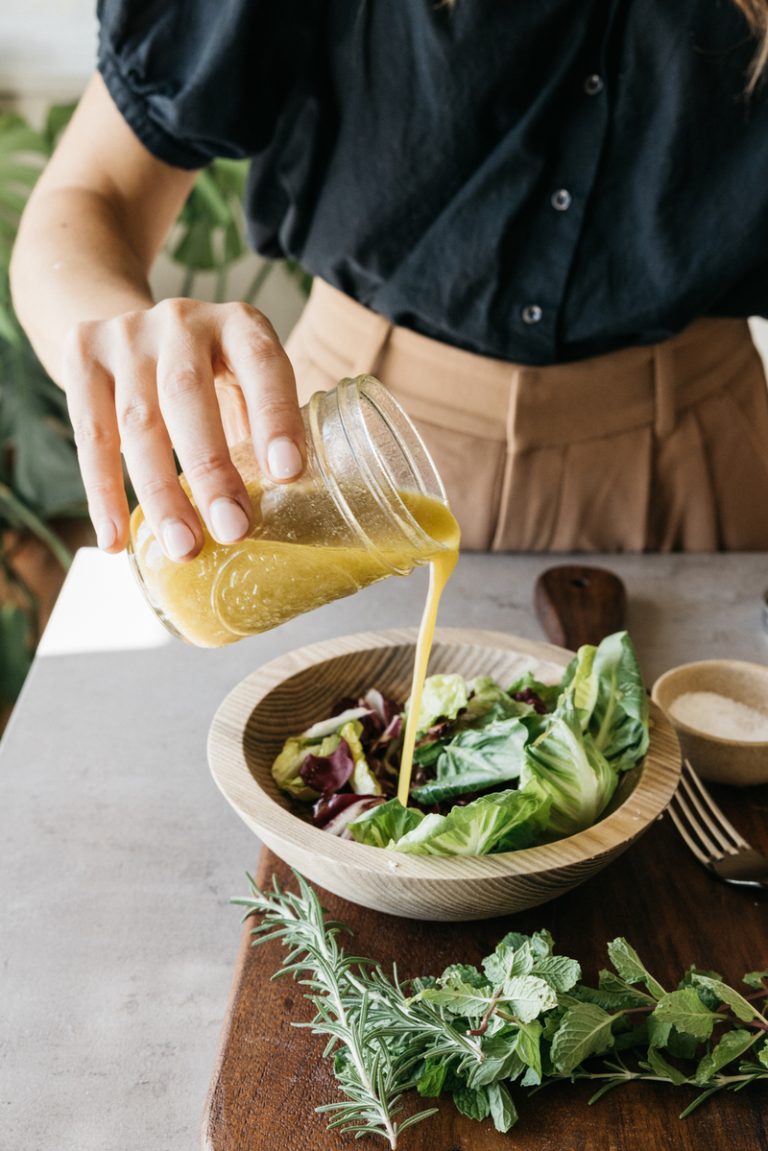 pouring vinaigrette on salad how to add more dark leafy greens to your diet