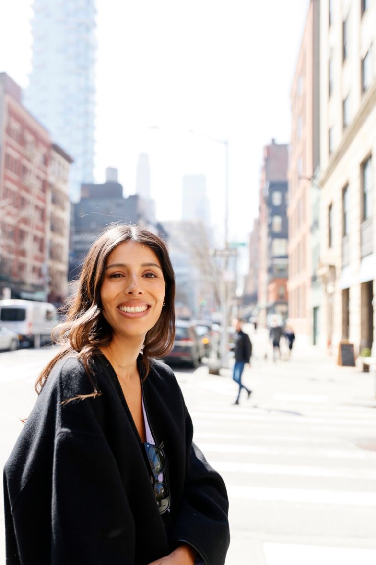 A woman smiling outside the city.