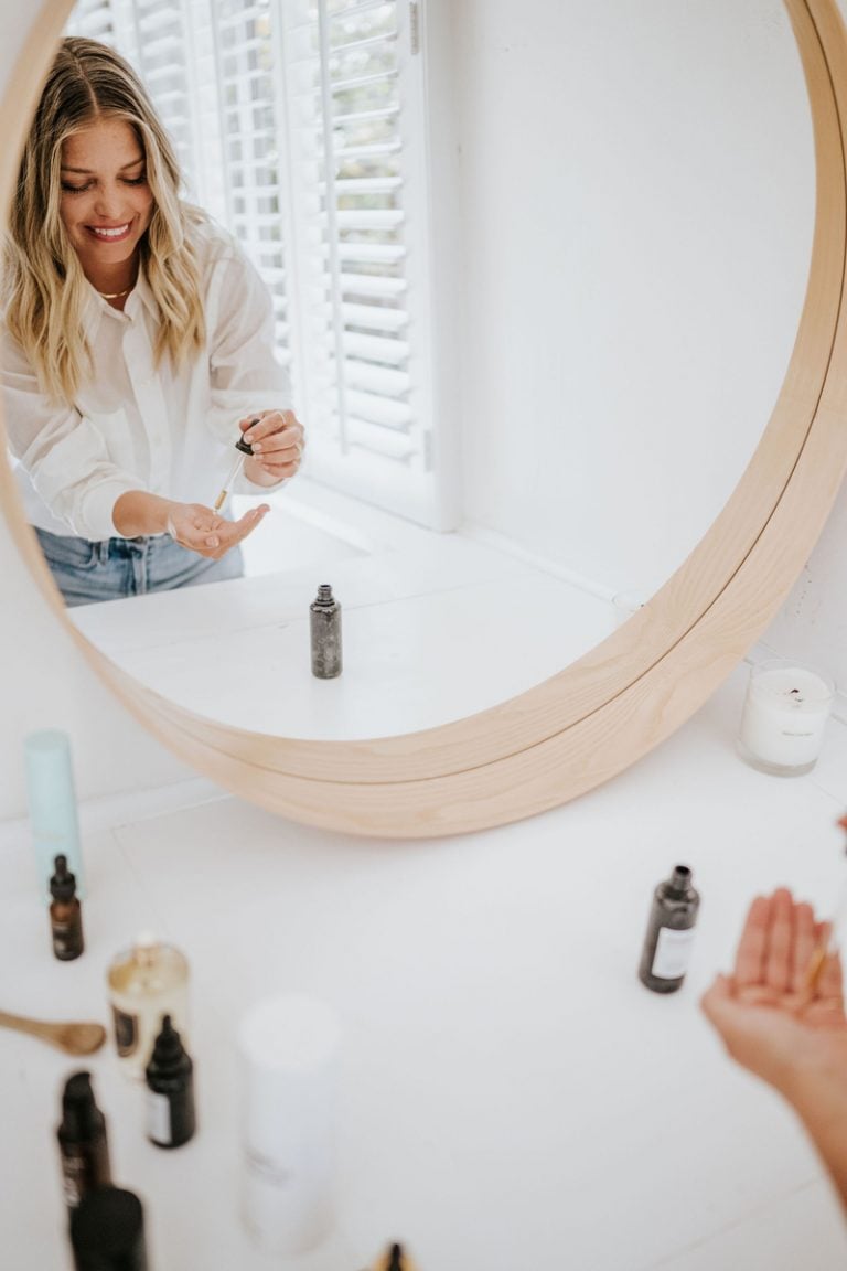 woman applying skincare in mirror best exfoliating face washes