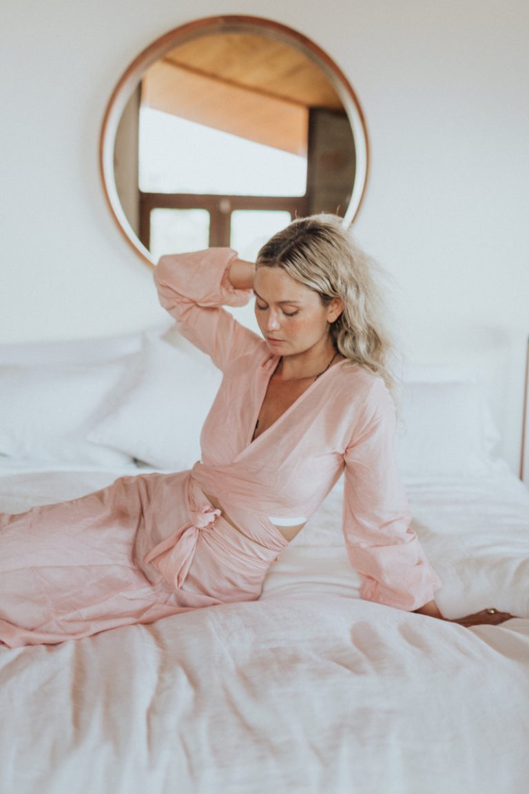 ผู้หญิงสวมชุดนอนสีชมพูนั่งอยู่บนเตียง