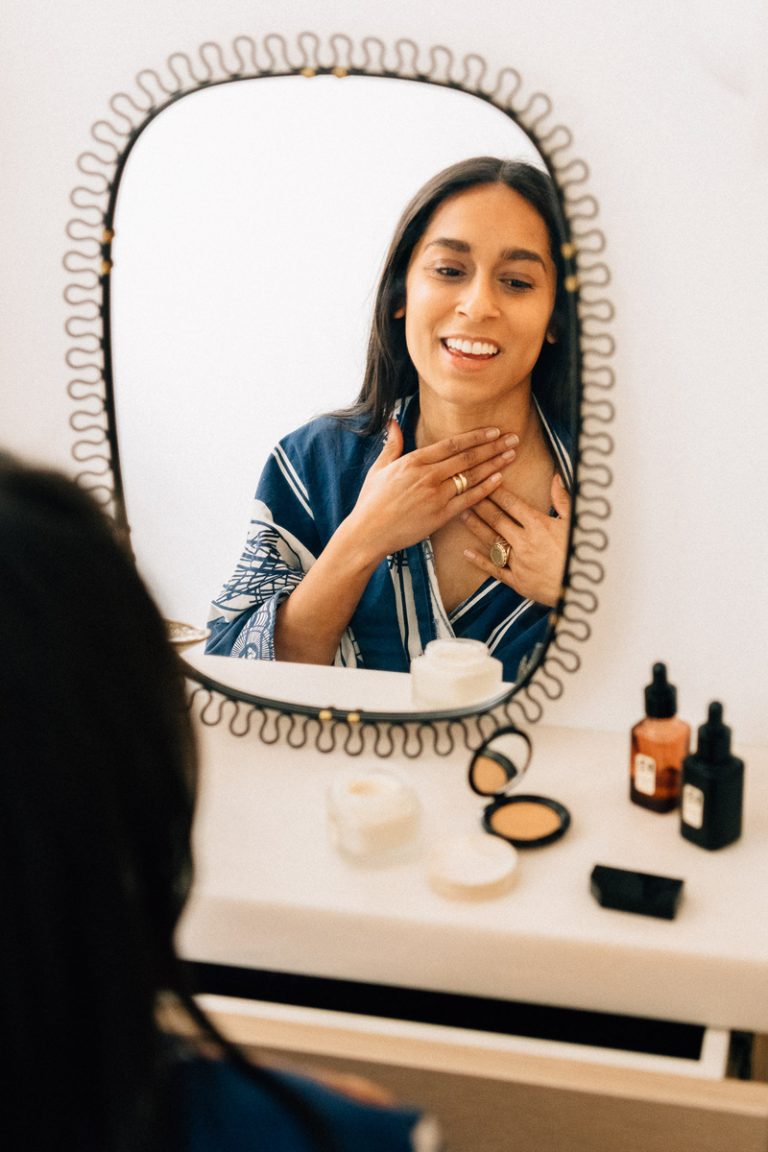 A woman applying skin care products in front of a mirror.