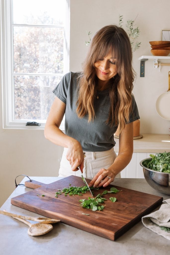 Brunette woman chopping herbs, fresh spring produce, greens, meal prep, kitchen, casa zuma gathering board