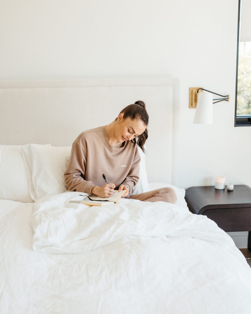woman wearing pink sweatsuit journaling in bed journal prompts