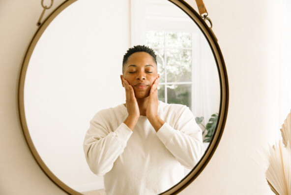 Woman applying skincare products in mirror.