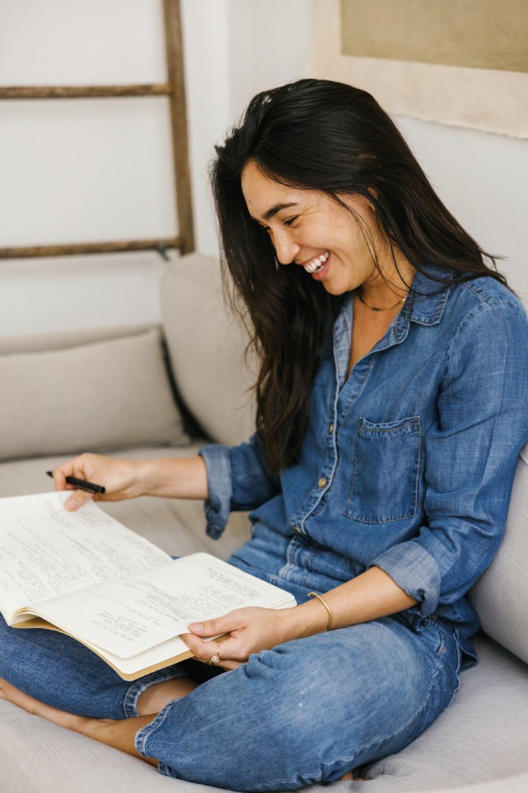 Woman wearing denim shirt and jeans reading through journal.
