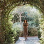 woman wearing dress walking under greenery arch