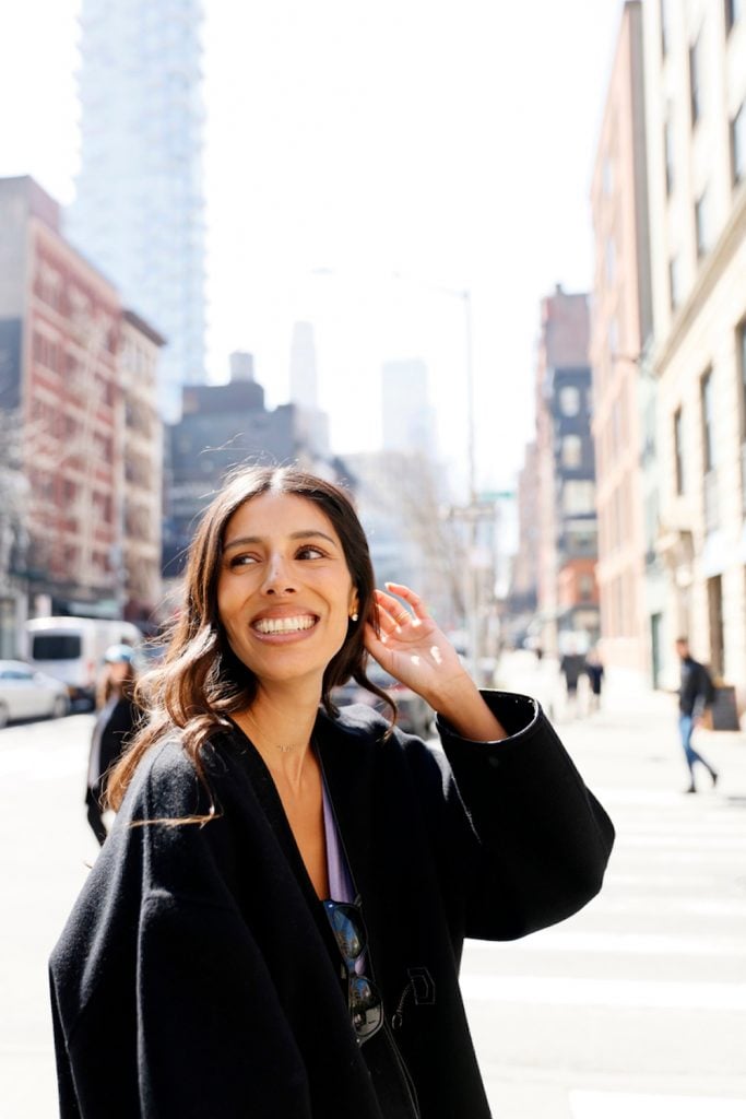 Brunette woman walking in the city wearing black cote smiling.